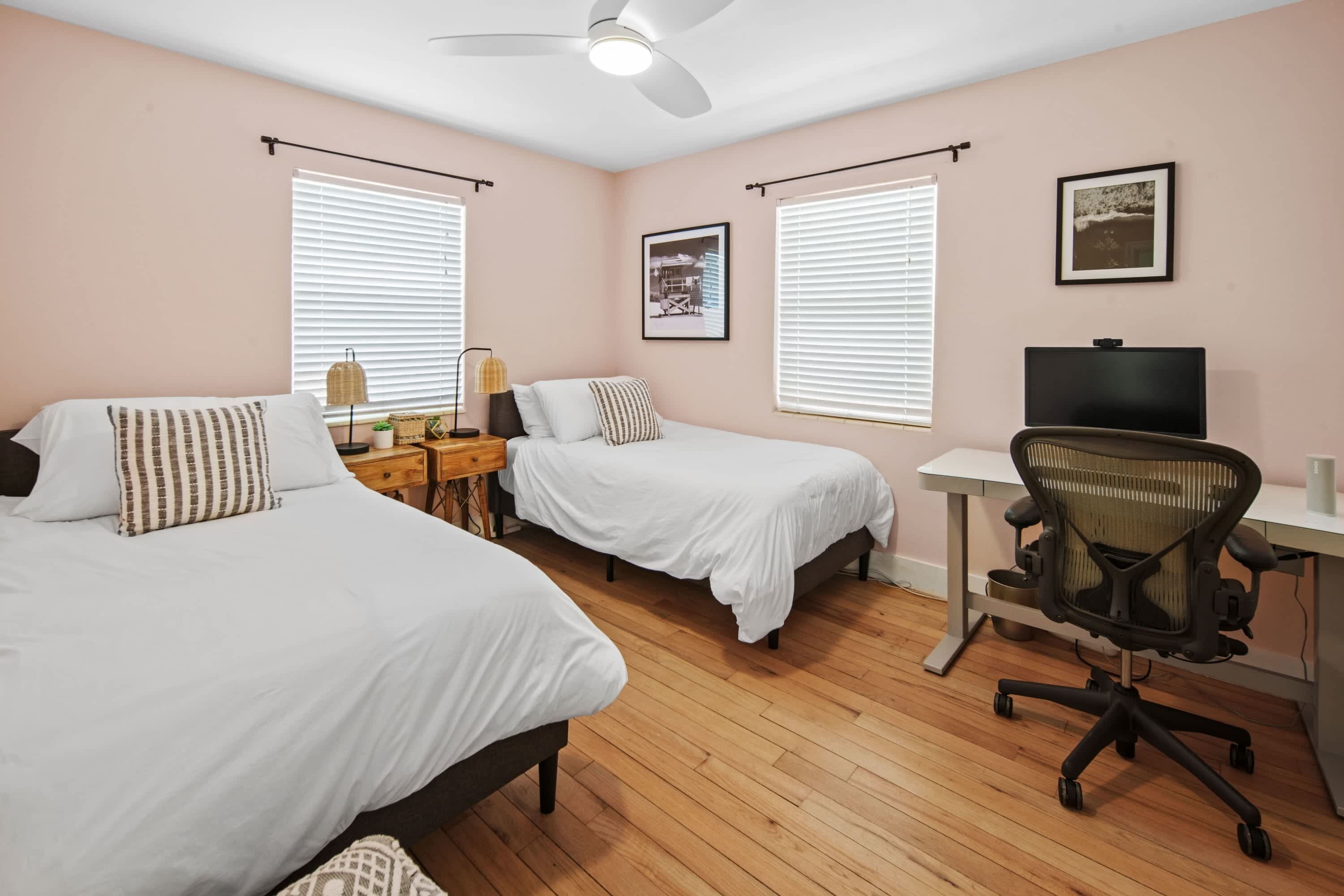 A bedroom with two beds, a desk, a chair, and a ceiling fan.