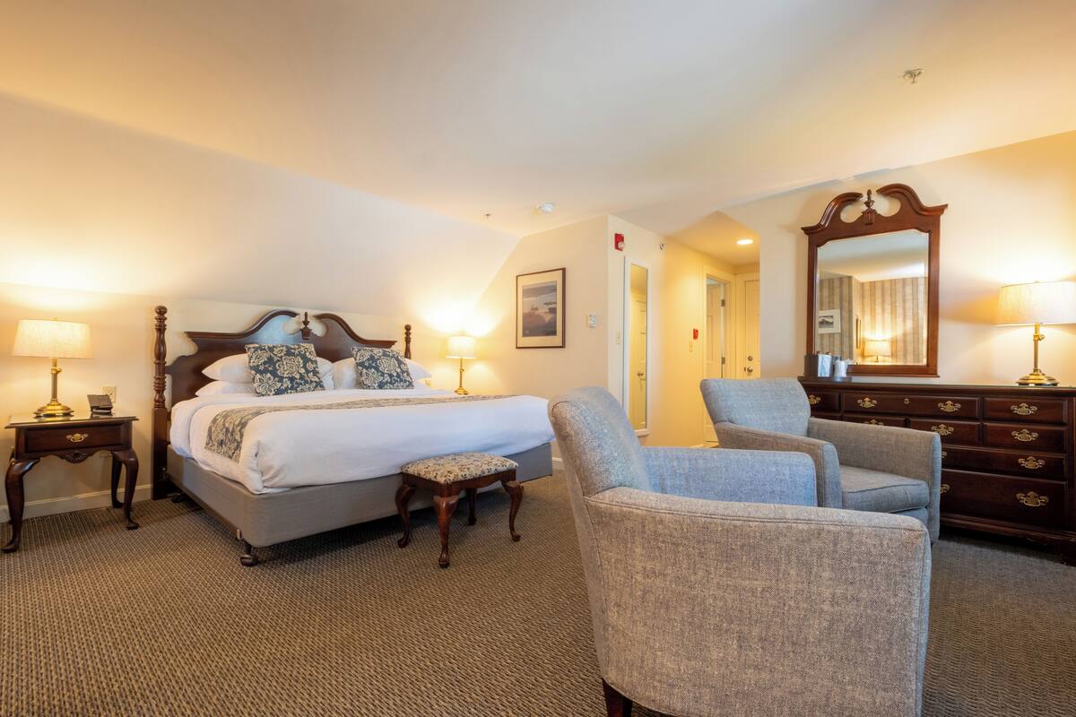 A hotel room with a bed, two bedside lamps, a chair, a dresser, and a mirror.