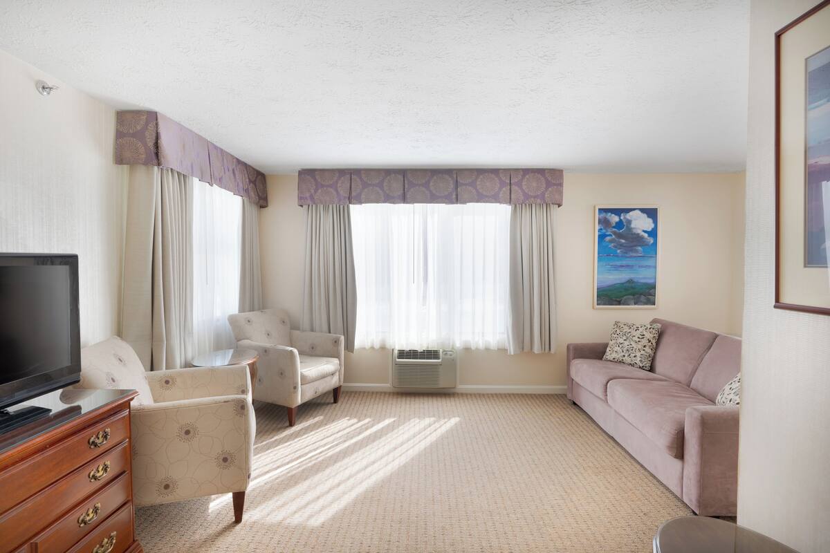 A hotel room with a television, two armchairs, a sofa, a dresser, and a painting on the wall.