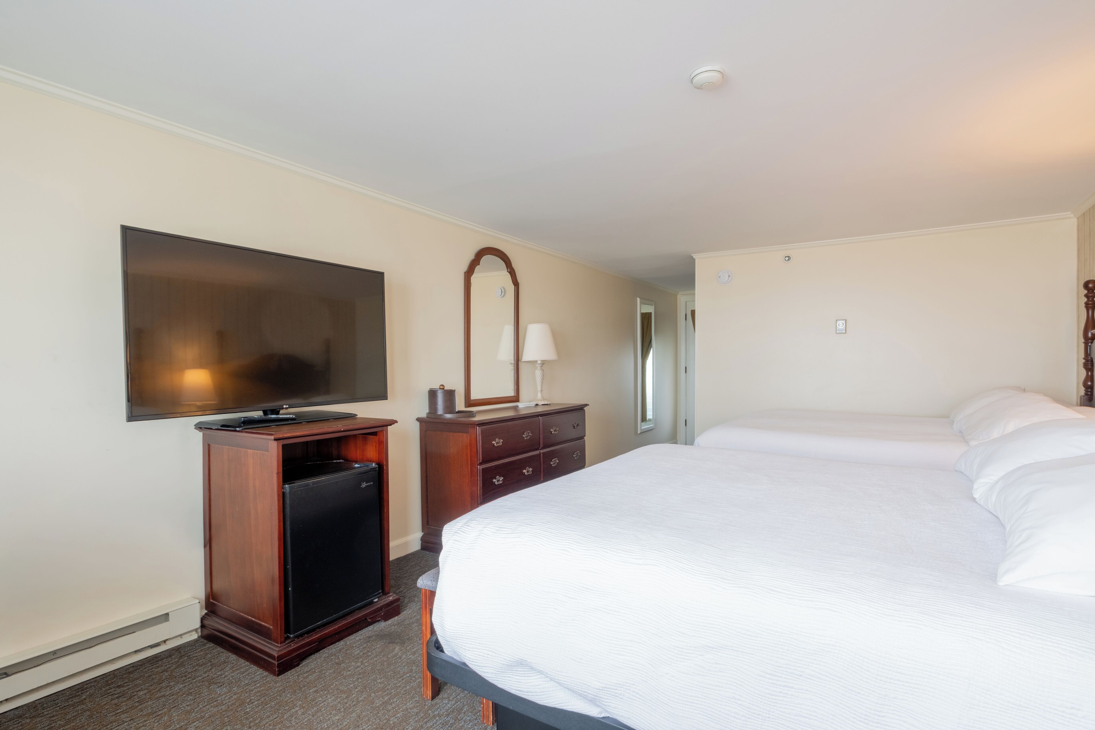 A hotel room with a large bed, a television, a dresser, and a mirror.