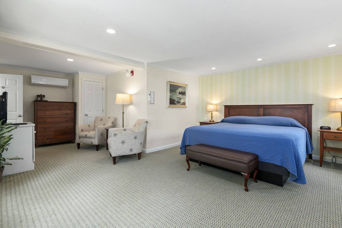 A hotel room with a large bed, a desk, a chair, a dresser, and a lamp.
