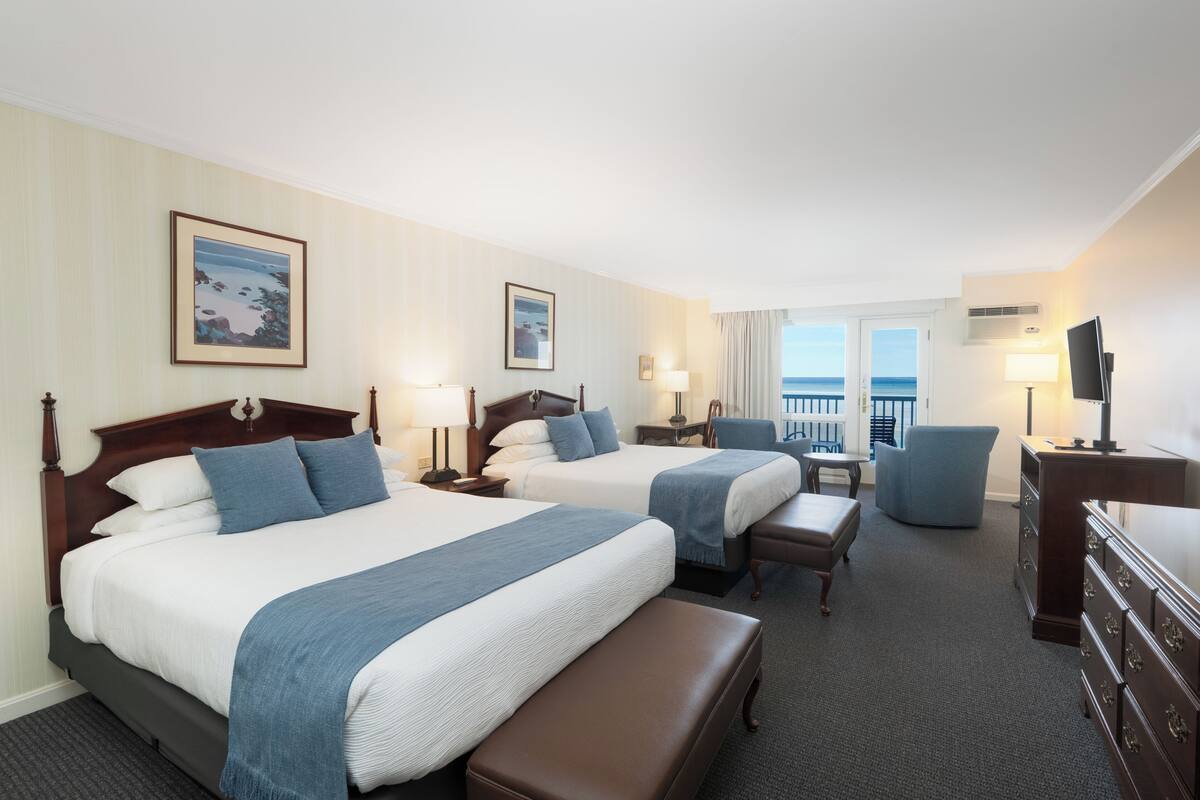 A hotel room with two beds, a desk, a chair, a dresser, and a view of the ocean.