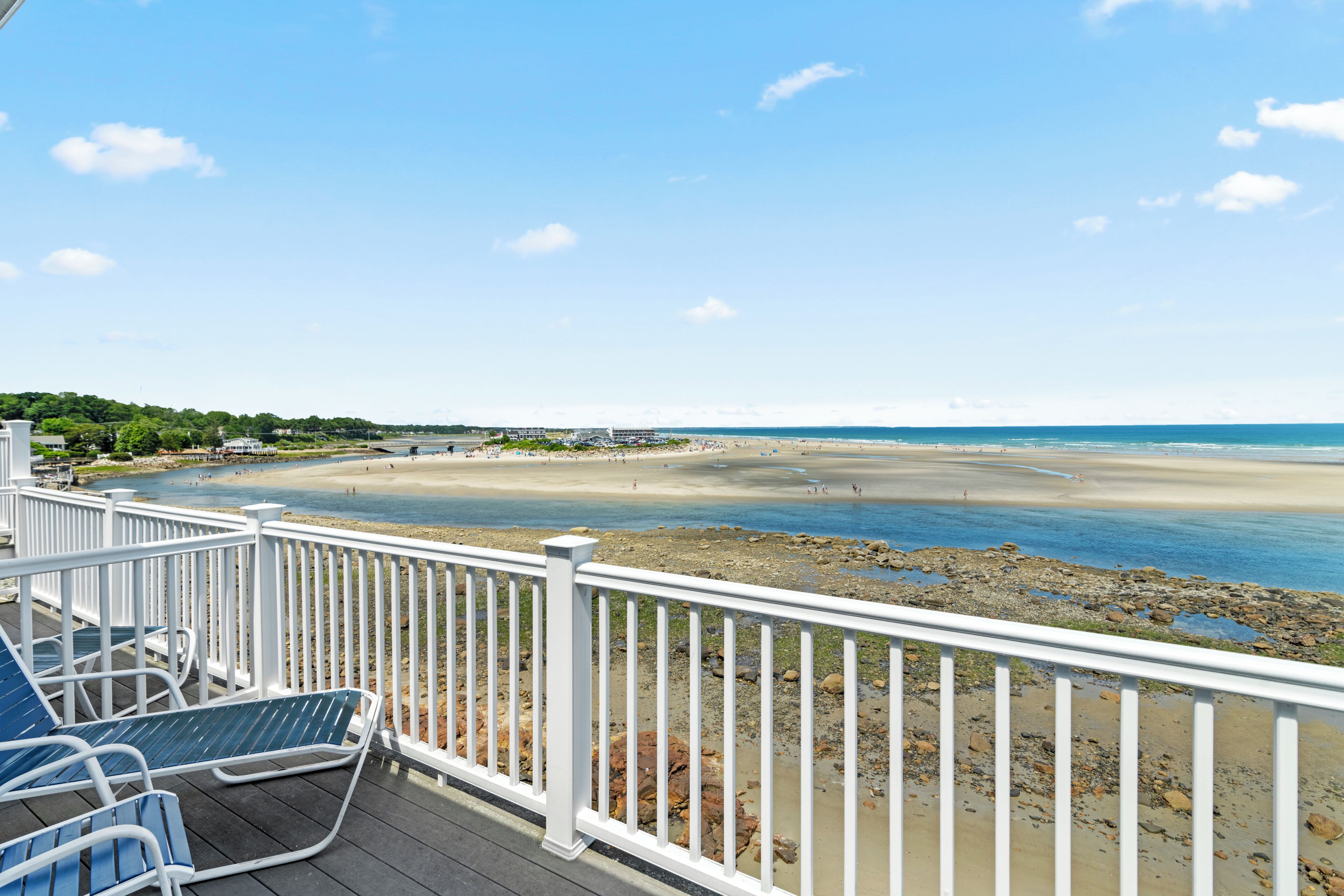 A beach view from a deck with white railings, a sandy beach, and a calm sea.