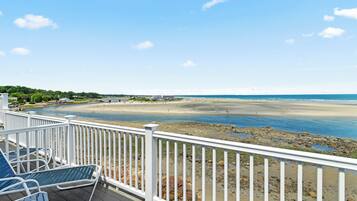 A beach view from a deck with white railings, a sandy beach, and a calm sea.