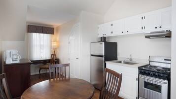 A compact kitchen with white cabinets, a stainless steel refrigerator, a stove, and a dining table with chairs.