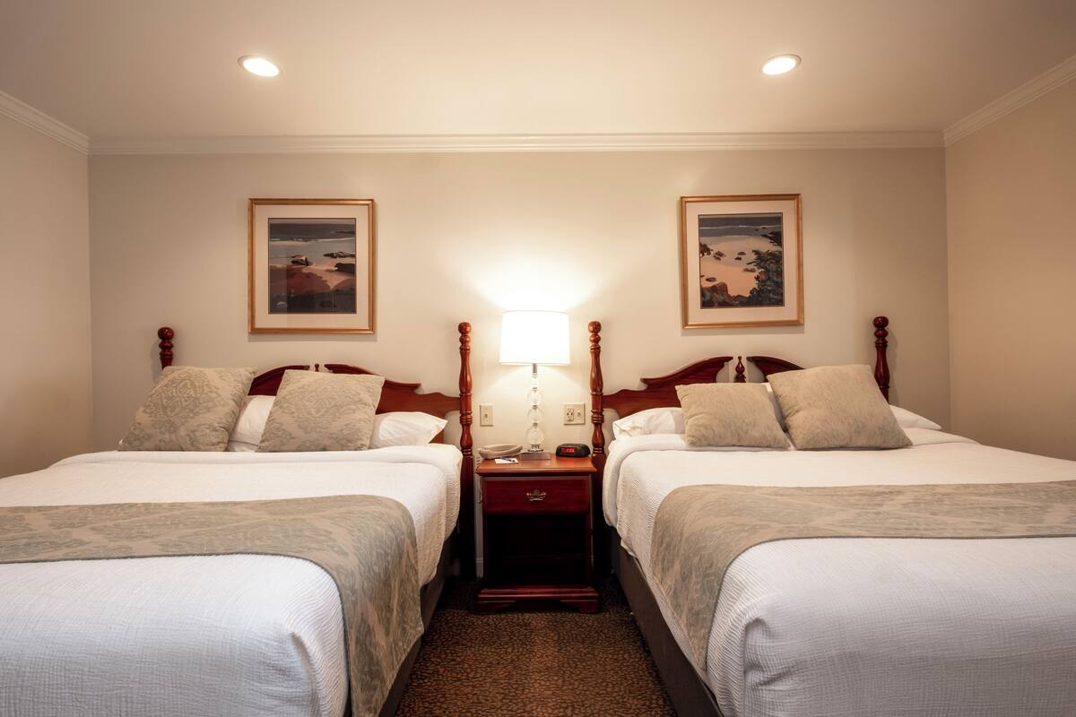 A hotel room with two beds, a nightstand with a lamp, and framed pictures on the walls.
