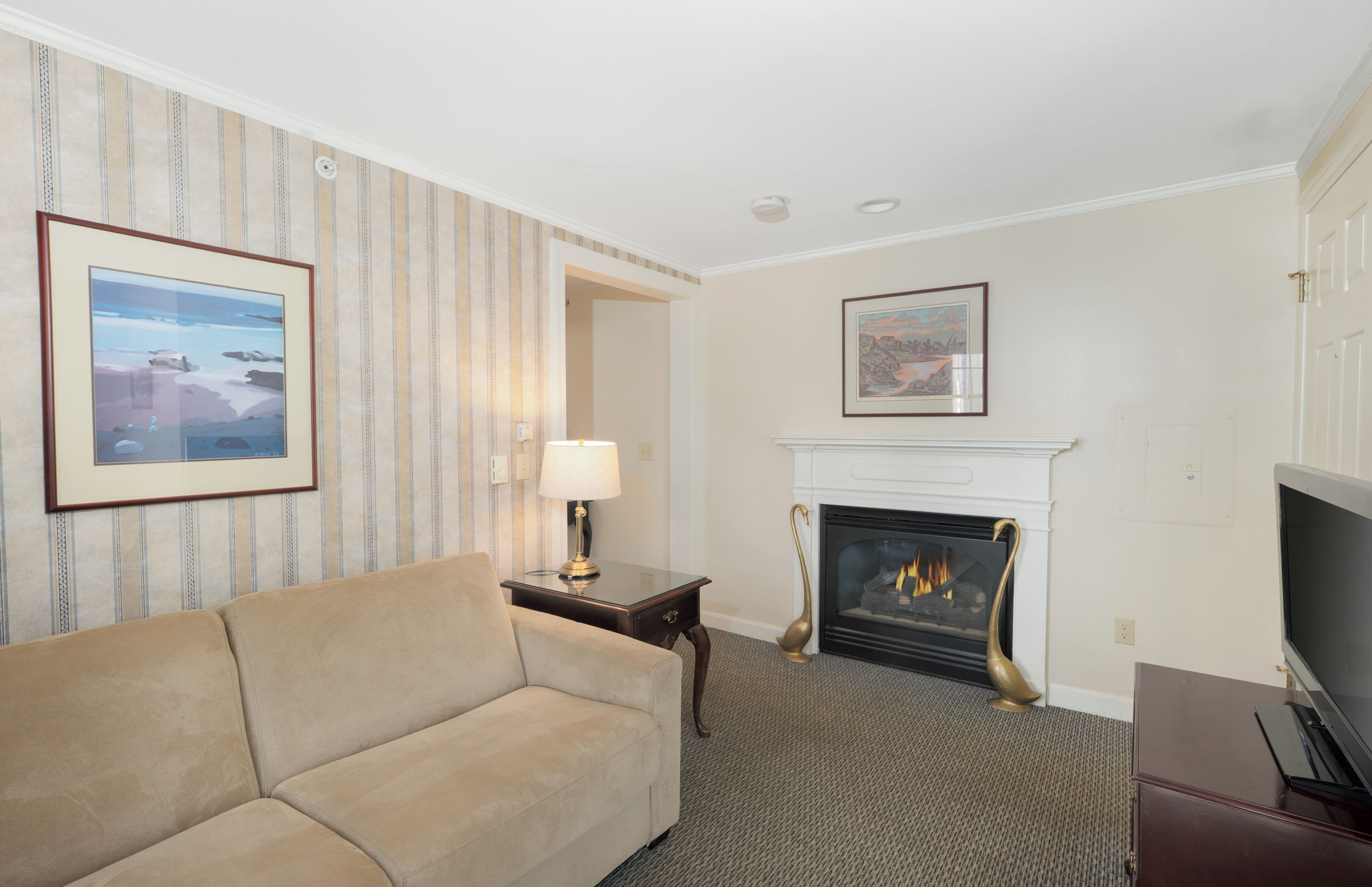 A living room with a sofa, a fireplace, a television, and framed artwork on the walls.