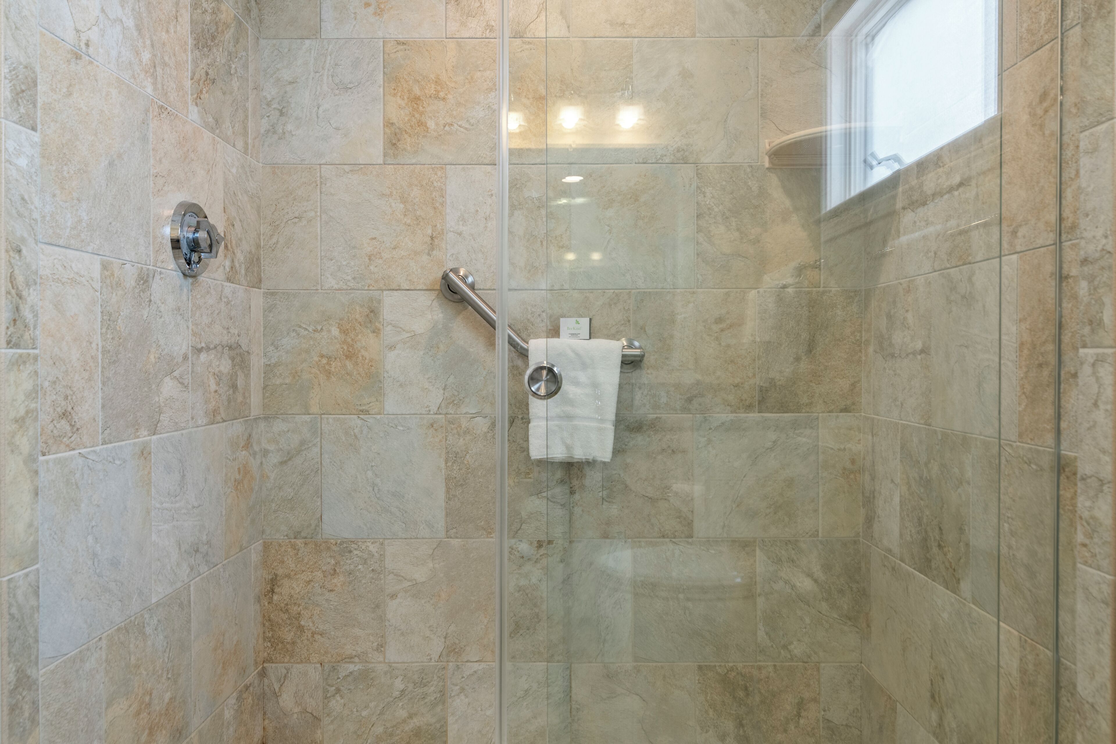 Ducha con puerta de vidrio, toallero y barra de apoyo.