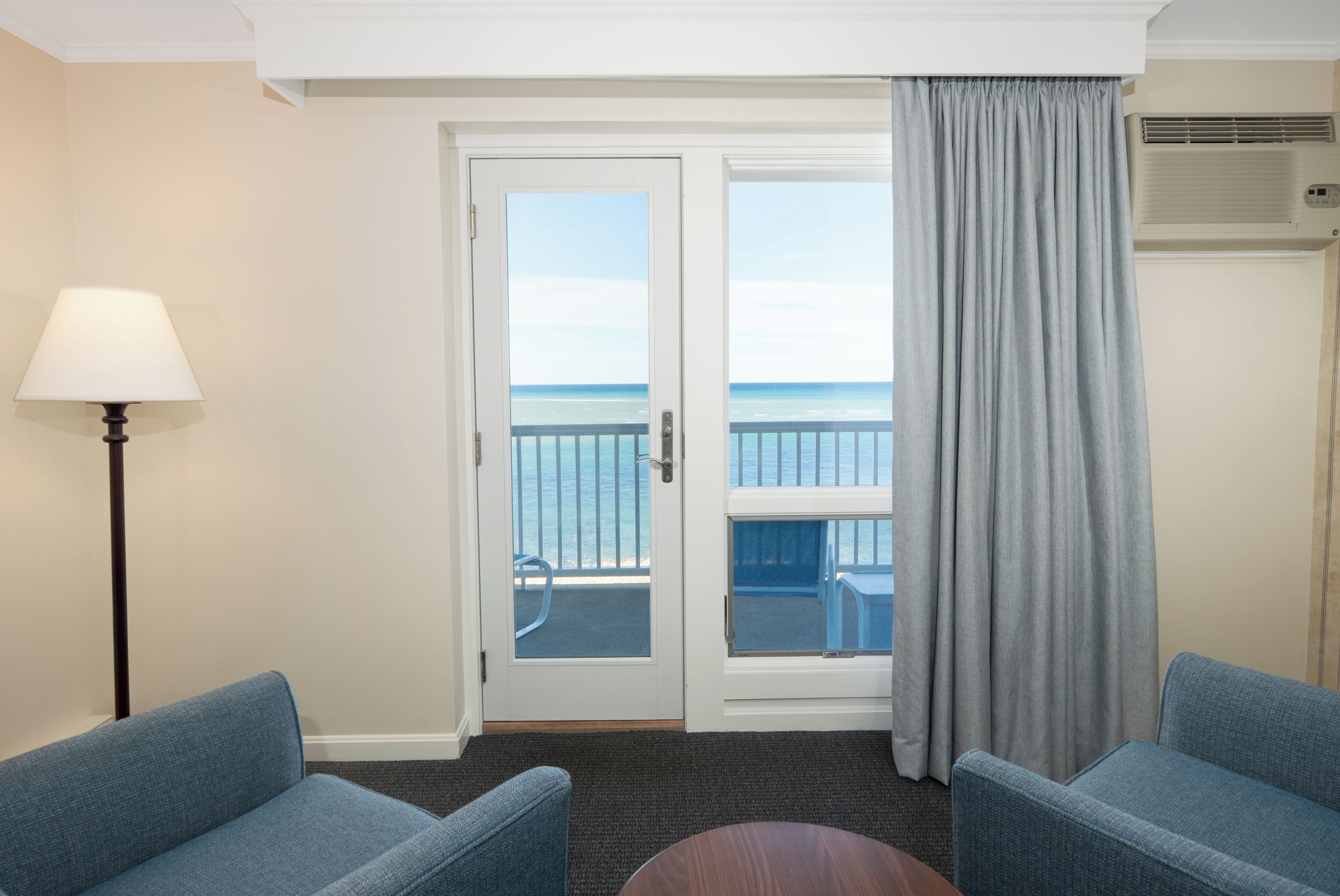 A room with a view of the ocean, a door with glass panels, a lamp, and two blue chairs.