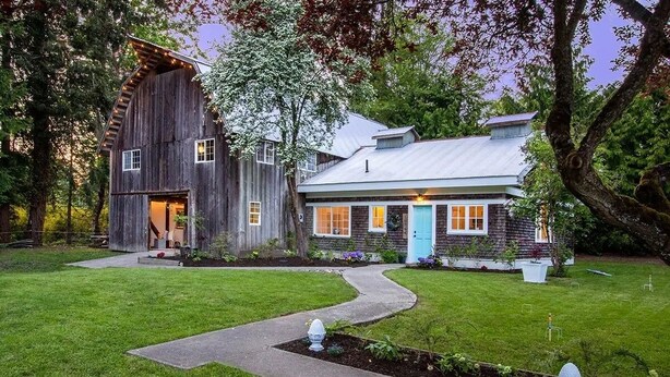 A rustic two-story house with a large barn-like structure on the left and a smaller house with a blue door on the right.