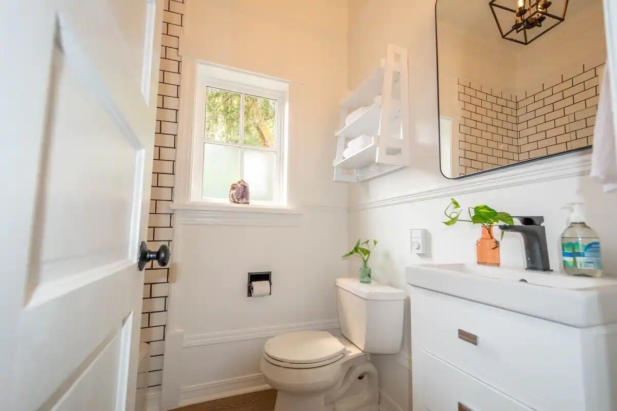 Une salle de bain comprenant des toilettes, un lavabo avec un miroir au-dessus, une fenêtre donnant sur des arbres et un porte-serviettes.
