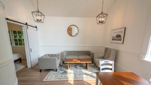 A cozy living room with a sofa, a coffee table, and a wooden bench. There is a mirror on the wall and a framed picture above the sofa.