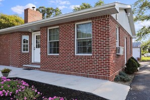 A two-story brick house with a front door, two windows, a chimney, and a small porch. - Lovely, Country Apartment, Just Minutes From Town. (Chambersburg)