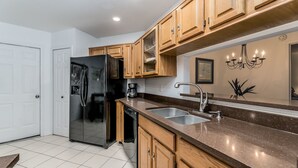 A modern kitchen with wooden cabinets, a stainless steel refrigerator, a double sink, and a chandelier.