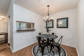 A dining area with a round table, chairs, a chandelier, and artwork on the walls.