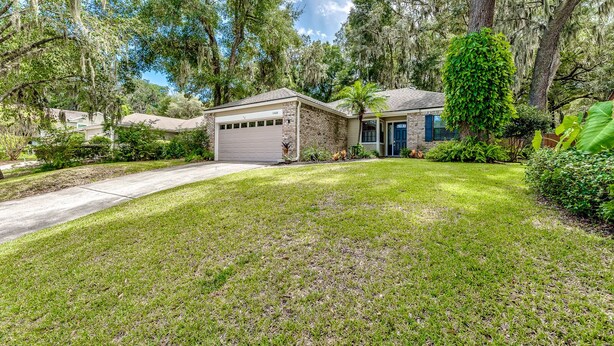 A residential house with a garage, a well-maintained lawn, and mature trees with Spanish moss.