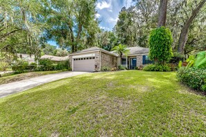 A residential house with a garage, a well-maintained lawn, and mature trees with Spanish moss.