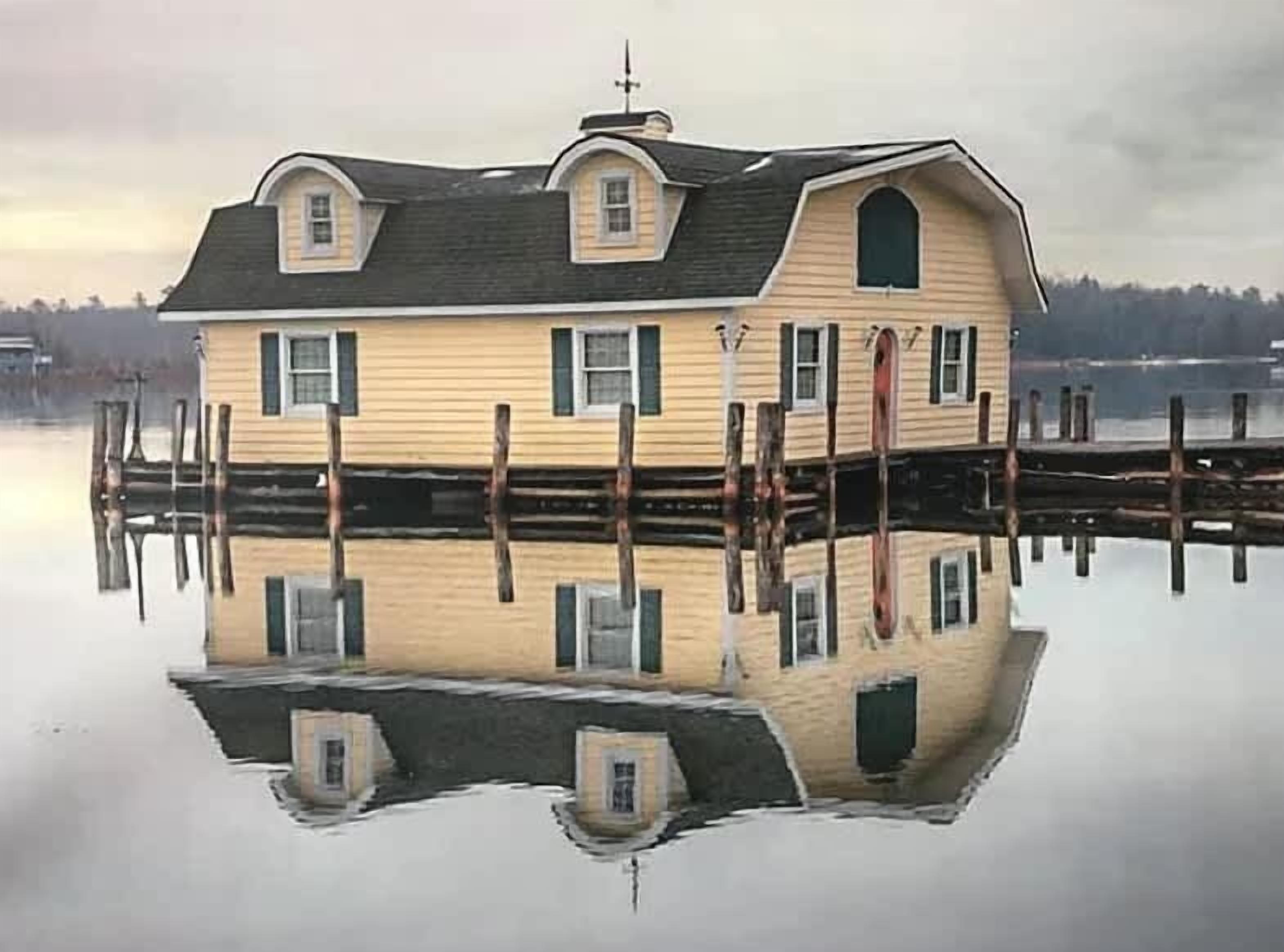 A house with a symmetrical design, featuring a central entrance and two side windows, surrounded by a dock extending into a calm body of water.