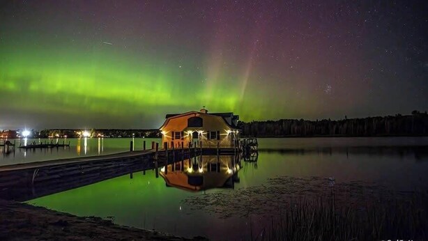 Et hus ved en rolig sø om natten med nordlys på himlen.