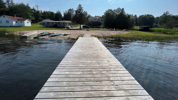 A wooden dock extending into a body of water with houses in the background. - 'Lakeside' Cottage with porch and sandy beach (Cedarville)