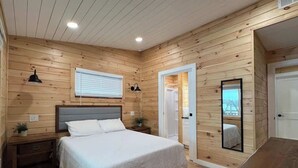 A wooden-paneled bedroom with a bed, bedside tables, a mirror, and a window. - 'Lakeside' Cottage with porch and sandy beach (Cedarville)