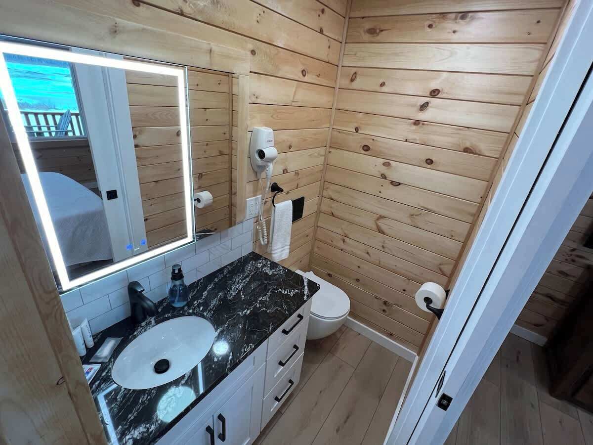 A compact bathroom with wooden walls, a marble sink, a toilet, and a mirror.