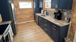 A modern kitchen with dark cabinets, a granite countertop, stainless steel appliances, and a window providing natural light. - 'Lakeside' Cottage with porch and sandy beach (Cedarville)