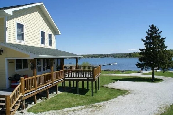 A house with a deck overlooking a lake, a gravel driveway, and a grassy area. - 'Northside' Cottage w screened in porch (Cedarville)