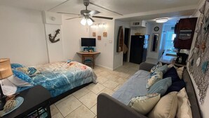 Una habitación pequeña con cama, escritorio, sofá y ventilador de techo.