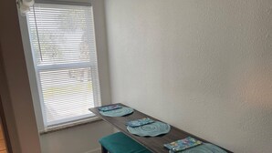 Un comedor con mesa y banco de madera, una ventana con persianas y una pared blanca.
