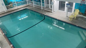 Una piscina interior con agua cristalina, rodeada por una cerca blanca y un mural con paisaje submarino.