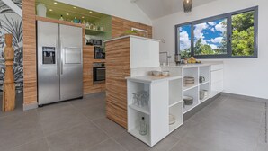 Een moderne keuken met een inbouwkoelkast, oven en magnetron, witte kasten en een raam met uitzicht op bomen.