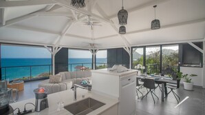Een moderne keuken met uitzicht op de oceaan, een eetgedeelte en een zithoek met een bank en tafel.