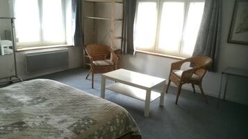 Ein Hotelzimmer mit einem Bett, einem kleinen Tisch, zwei Korbstühlen, einem Kleiderschrank und einem Fenster mit Vorhängen.