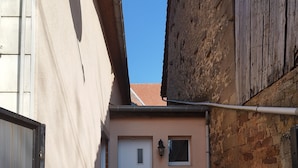 Une petite terrasse extérieure avec une table et des chaises, une porte et un mur avec une fenêtre.