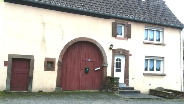 Un bâtiment à deux étages avec une porte rouge, une petite fenêtre et une boîte aux lettres.