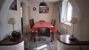 Un coin repas avec une table rouge, des chaises noires, un luminaire suspendu noir et une horloge au mur.