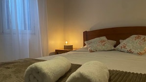 Un lit bien fait, avec des serviettes blanches pliées en rouleaux, une tête de lit en bois et des coussins à motifs floraux.