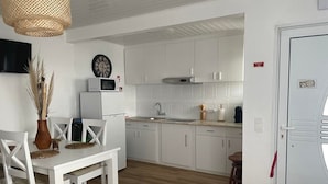 Une cuisine moderne avec des meubles blancs, un four à micro-ondes et un coin repas comprenant une table et des chaises blanches.