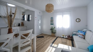 Un salon moderne avec un canapé blanc, une table à manger avec des chaises, un coin cuisine et un luminaire suspendu.