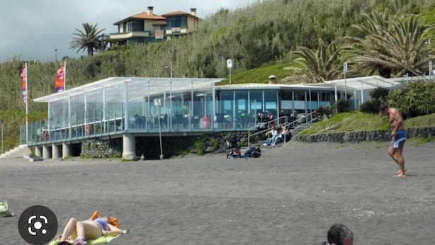 Un bâtiment situé en bord de mer, doté d’une façade en verre, d’une allée couverte et surplombant une colline.