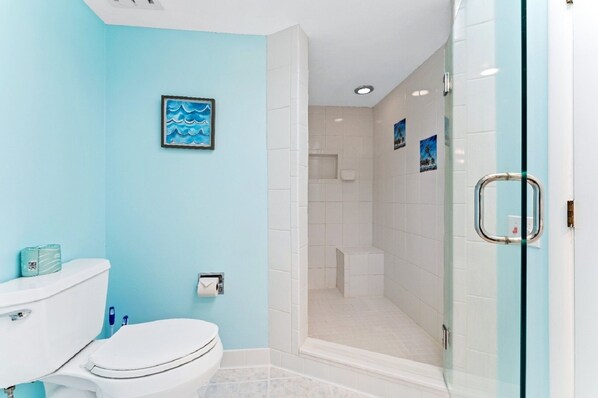 Une salle de bain comprenant des toilettes, un lavabo, une douche et un espace de douche séparé par une paroi en verre.