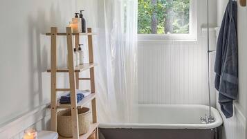 Een badkamer met een badkuip, toilet en een raam met uitzicht op groen.