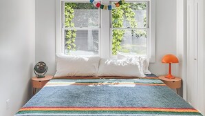 A bedroom with a bed, two windows, a fan, a lamp, and a ceiling light fixture.