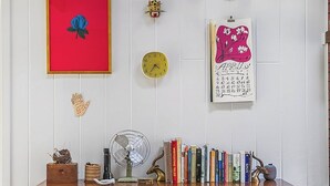 A room with a white wall, a wooden floor, a white dresser, and various decorative items including a clock, a calendar, and framed artwork.