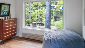 A room with a large window, a wooden dresser, a bench, and a framed picture on the wall.