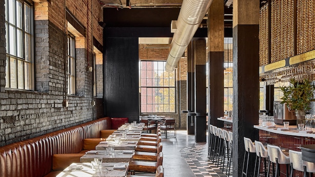 Un restaurant avec de longues tables communes, des banquettes, des murs en briques et un sol à carreaux.