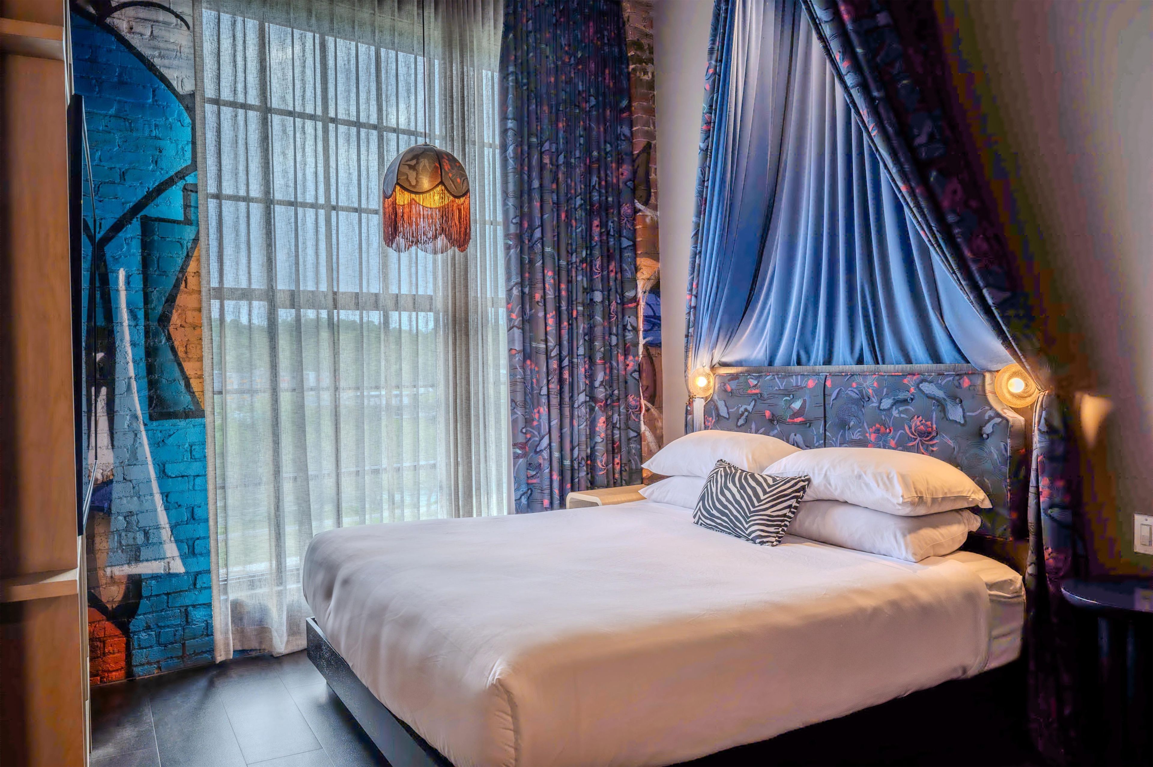 A bedroom with a bed, curtains, a hanging light fixture, and a wall with a floral pattern.