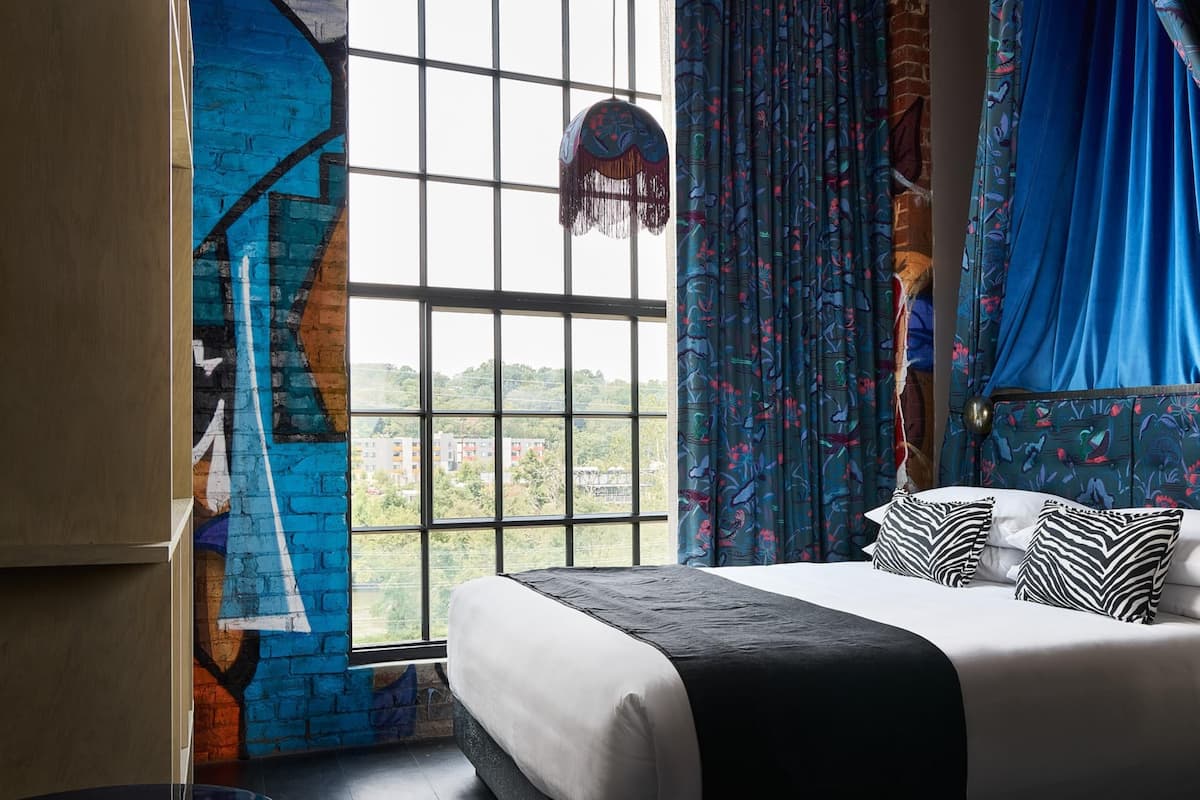 A bedroom with a large window, a bed with a black and white bedspread, and a blue curtain with a floral pattern.