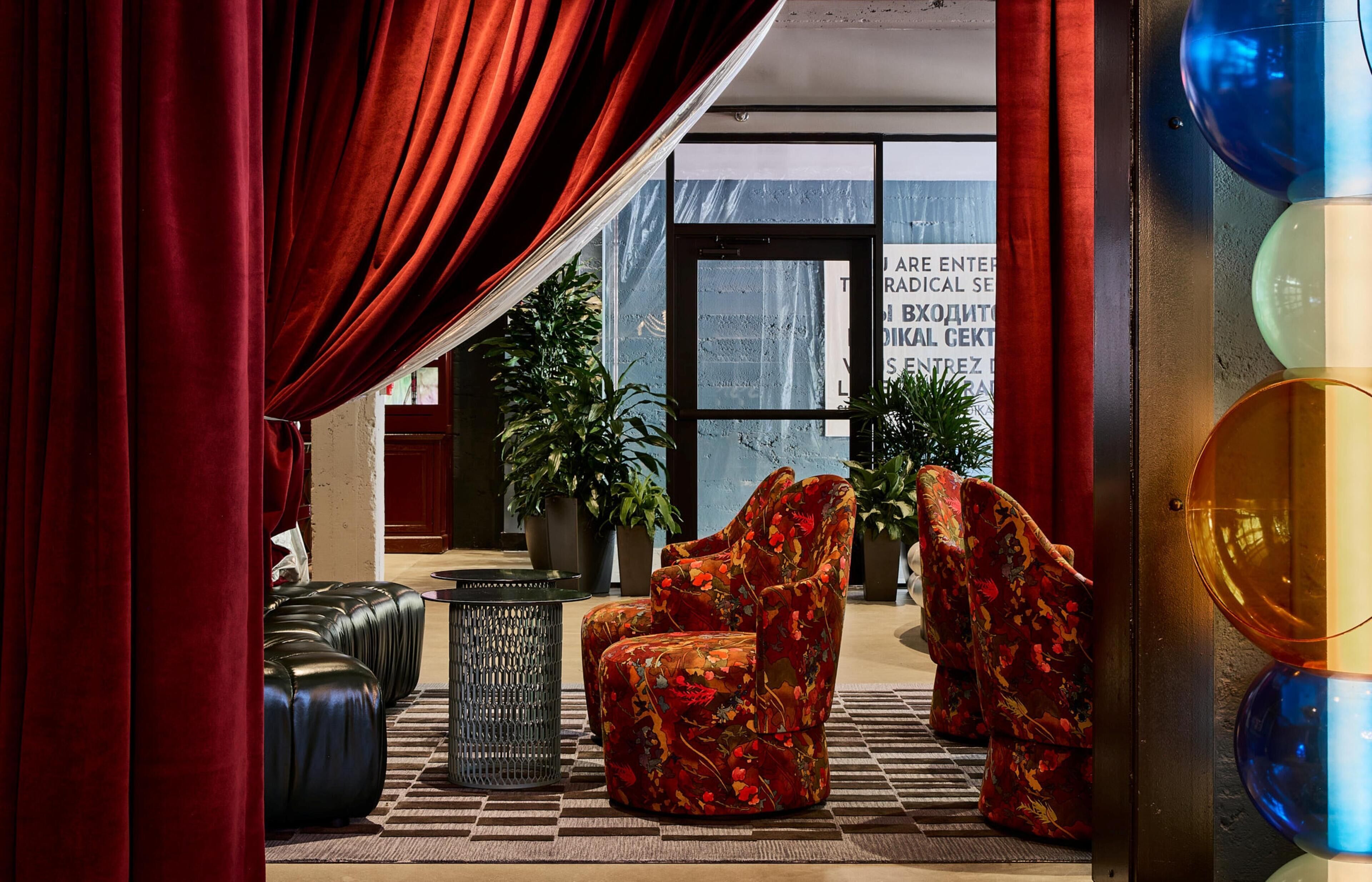 A lobby with red curtains, a sofa, a chair, and potted plants.